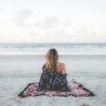 woman sitting on blanket located on shoreline