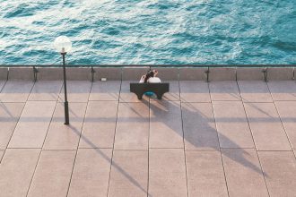 man in black shirt sitting on chair near swimming pool during daytime